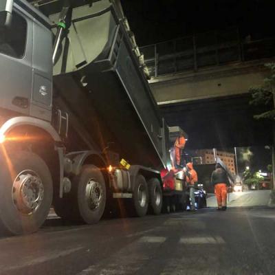 Fila di camion da trasporto asfalto in attesa vicino alla finitrice durante un grande cantiere stradale.