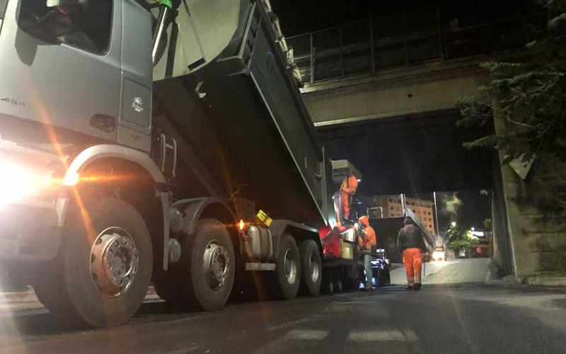 Fila di camion da trasporto asfalto in attesa vicino alla finitrice durante un grande cantiere stradale.